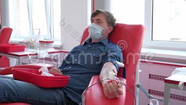 在<strong>献血</strong>中心戴医疗面罩的椅子上的男人。 <strong>献血</strong>者<strong>献血</strong>。 19大流行病